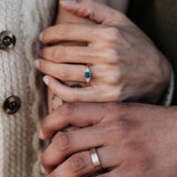 Close-up of two hands holding each other, one wearing a blue gemstone ring and the other a gold ring.