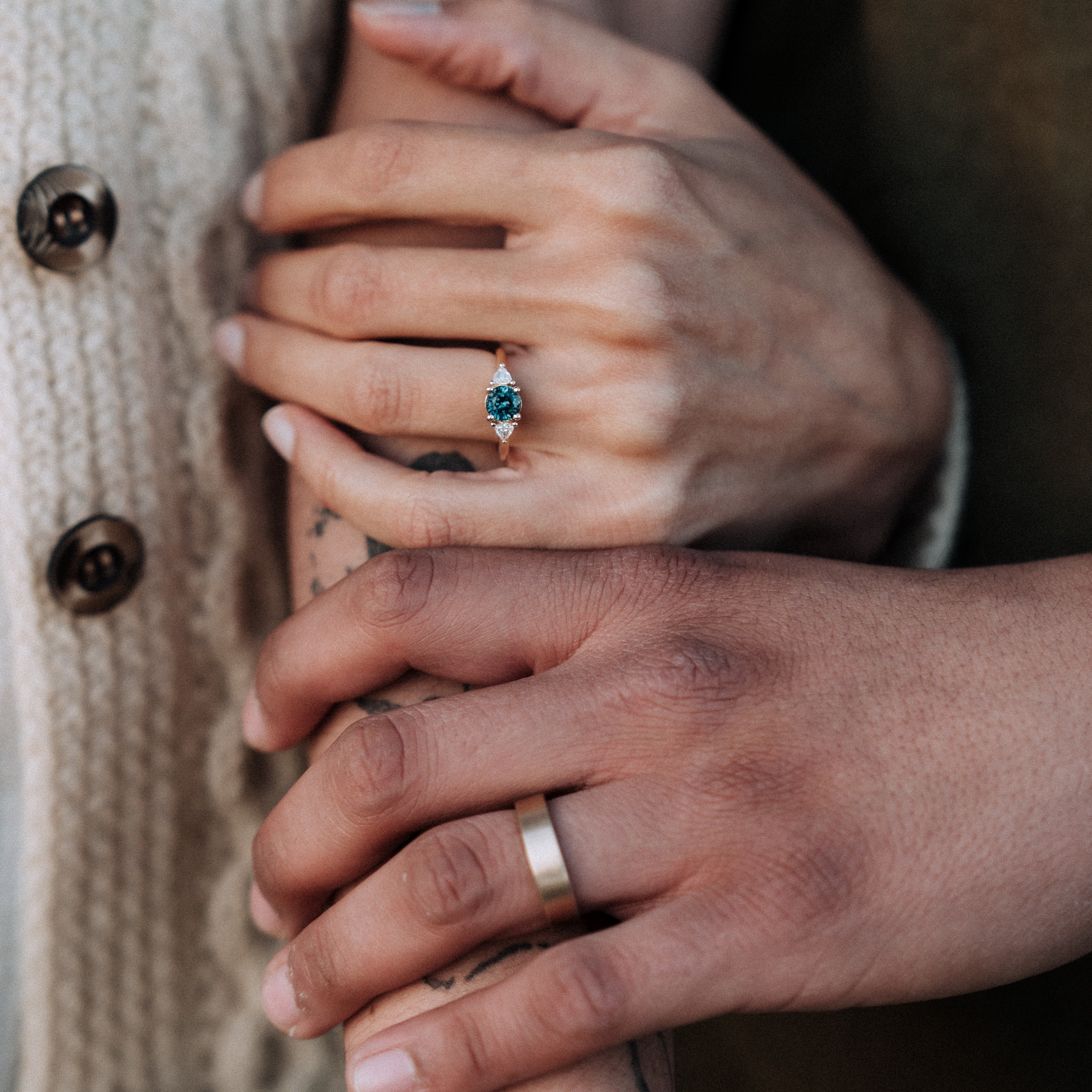 Close-up of two hands holding each other, one wearing a blue gemstone ring and the other a gold ring.