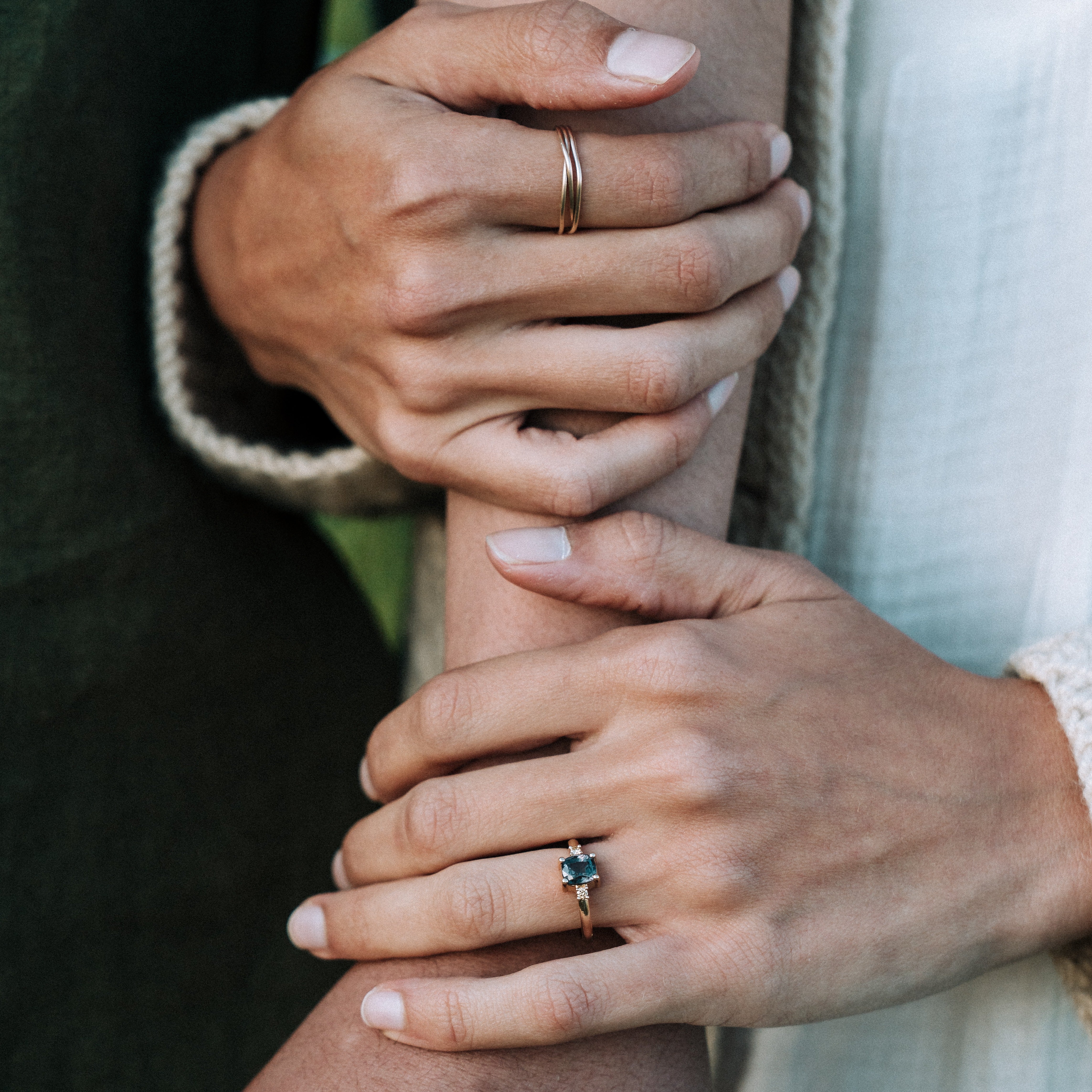 Close-up of two hands holding each other, one with a gold ring and the other with a blue gemstone ring.