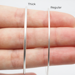 Two silver hoop earrings, one thick and one regular, on a hand against a white background.