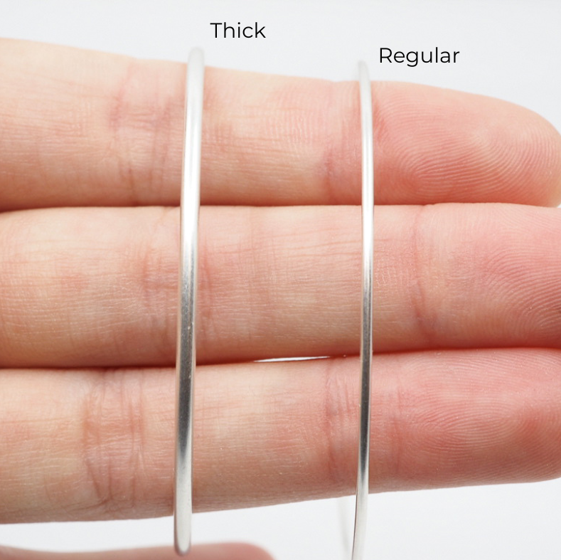 Two silver hoop earrings, one thick and one regular, on a hand against a white background.