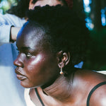 A close-up lifestyle shot of a woman with short black hair wearing a small silver hoop earring, with another person in a red patterned bandana in the background.