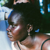 A close-up lifestyle shot of a woman with short black hair wearing a small silver hoop earring, with another person in a red patterned bandana in the background.