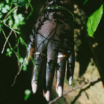 A close-up of a hand wearing silver rings, set against a dark background with green foliage.