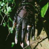 A close-up of a hand wearing silver rings, set against a dark background with green foliage.