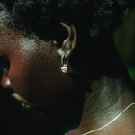 Close-up side profile of a person wearing a small silver hoop earring with a tiny orange and white stone, along with a thin silver necklace.
