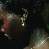 Close-up side profile of a person wearing a small silver hoop earring with a tiny orange and white stone, along with a thin silver necklace.