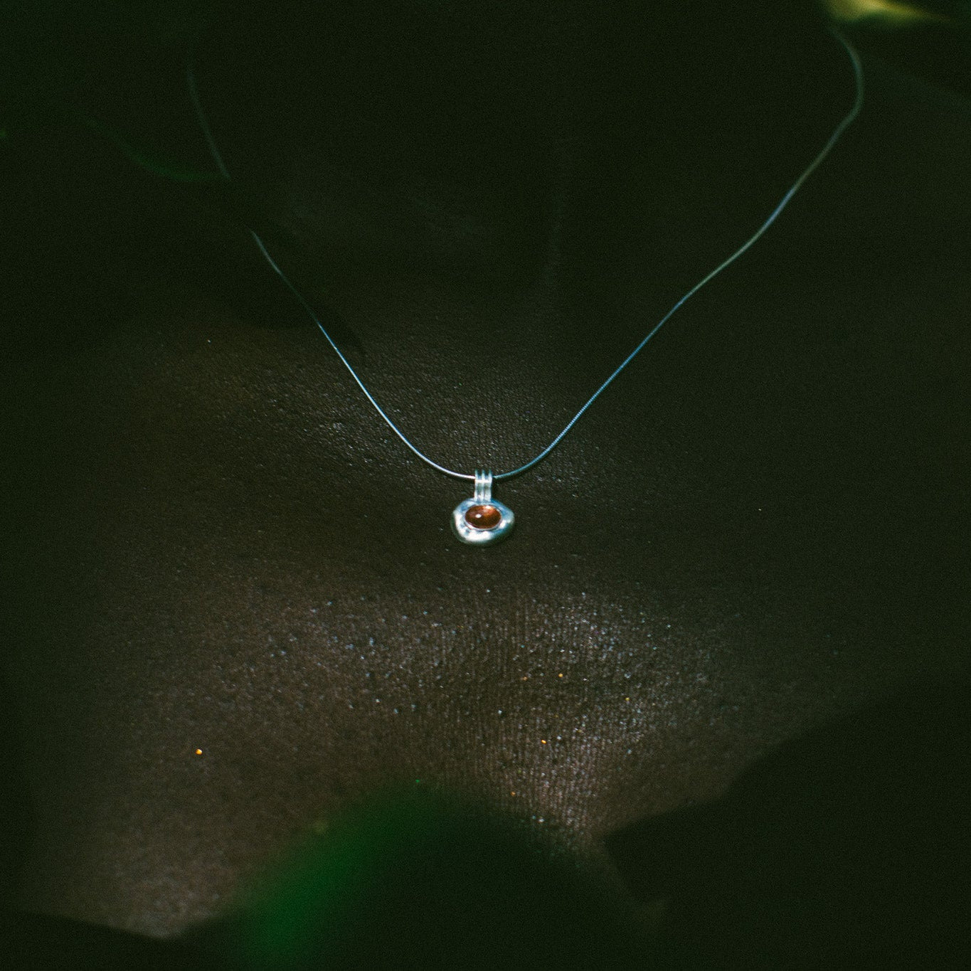 A delicate light blue necklace with a small heart-shaped pendant featuring a red heart and white outer heart, worn on a person's neck against a dark background.