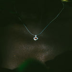 A delicate light blue necklace with a small heart-shaped pendant featuring a red heart and white outer heart, worn on a person's neck against a dark background.