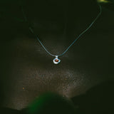 A delicate light blue necklace with a small heart-shaped pendant featuring a red heart and white outer heart, worn on a person's neck against a dark background.