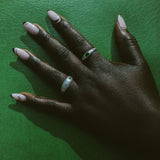A close-up of a hand wearing two silver rings against a textured green background.