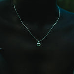 A close-up of a person wearing a delicate silver chain necklace with a small circular pendant featuring a green stone.
