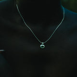 A close-up of a person wearing a delicate silver chain necklace with a small circular pendant featuring a green stone.
