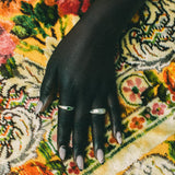 A close-up of a hand with silver rings, resting on a highly patterned, colorful woven rug.