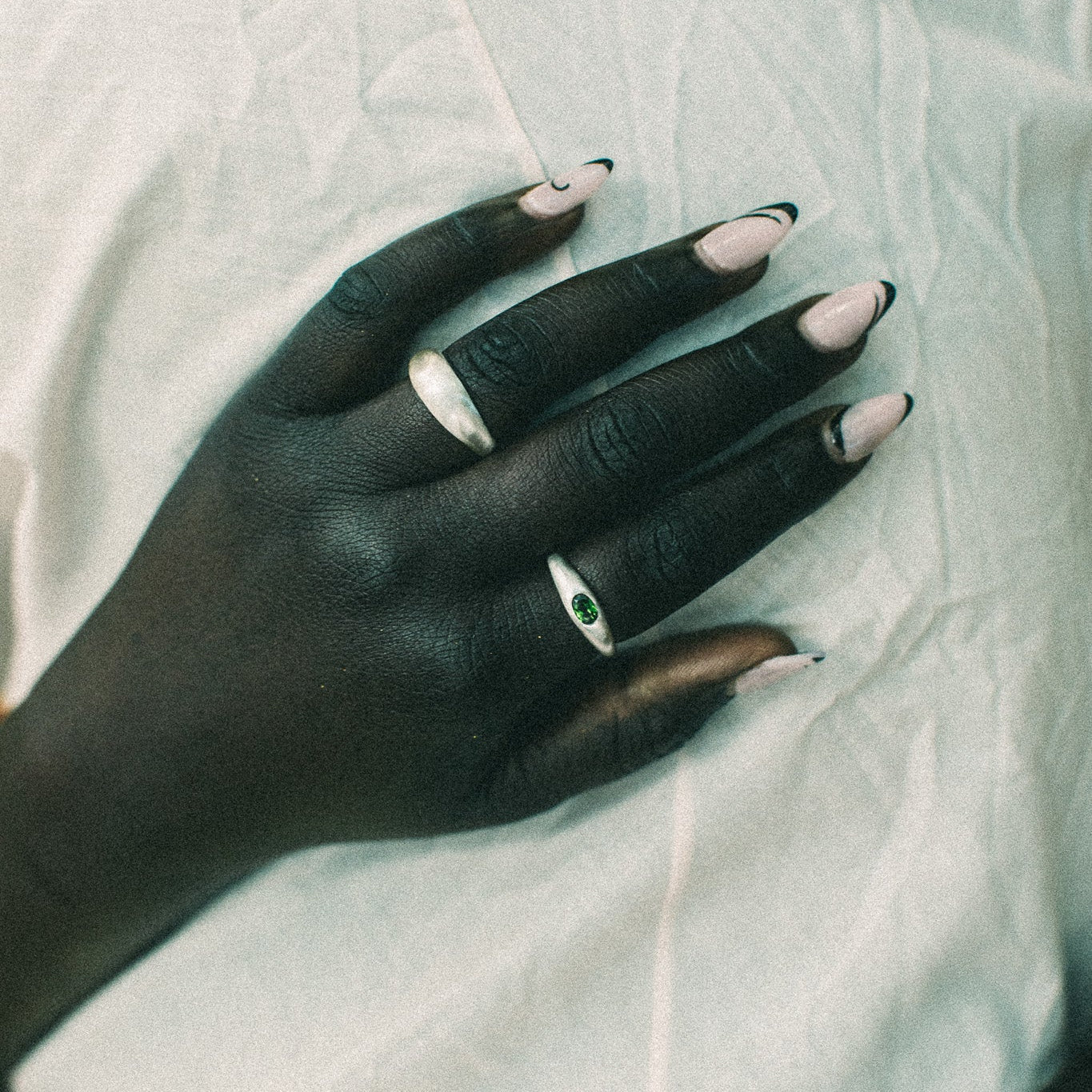 A close-up of a hand resting on a wrinkled white fabric, wearing two silver rings.