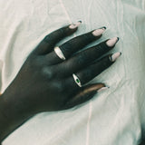 A close-up of a hand resting on a wrinkled white fabric, wearing two silver rings.
