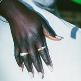 A close-up of a hand wearing two silver rings, resting on a white surface.