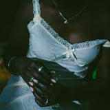 A close-up lifestyle shot of a person wearing a white lace-trimmed camisole top and white pants, adorned with silver rings.