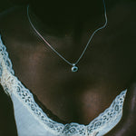 A close-up lifestyle shot of a person wearing a delicate silver chain necklace with a small round pendant, styled with a white lace-trimmed top.