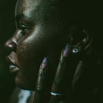 Close-up side profile of a person touching their face, wearing a small silver earring and a silver ring.