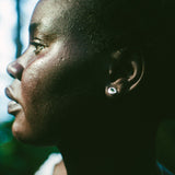 Close-up side profile of a person outdoors wearing a small round earring with a green center.