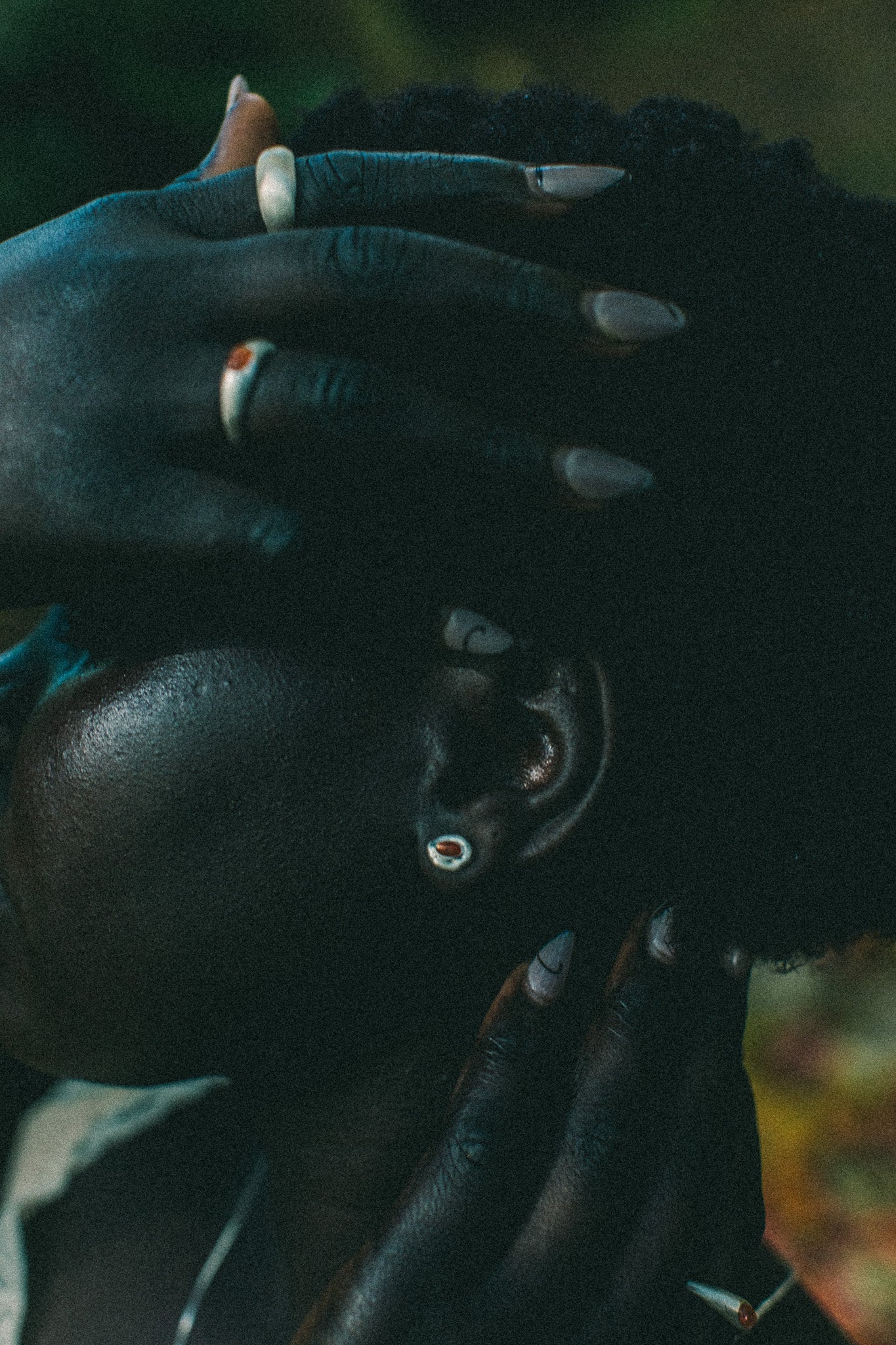 A close-up lifestyle shot of a person wearing silver-toned earrings and rings, with their hands resting on their head against a dark, blurred background.