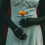 A person wearing a light blue lace-trimmed dress holds a single orange flower. The photo is cropped from the shoulders down, with dark background elements visible behind the subject.
