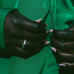 Close-up of a person wearing a vibrant green satin-like top or dress, with their hands buttoning the front. The person is wearing a silver ring with a green stone on one finger.
