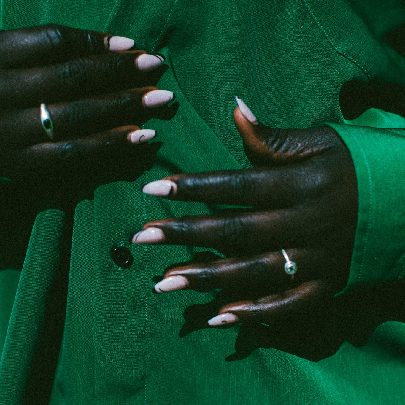 Close-up of a person wearing a bright green button-up shirt, showing both hands with pale pink manicured nails and rings.