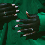Close-up of a person wearing a bright green button-up shirt, showing both hands with pale pink manicured nails and rings.