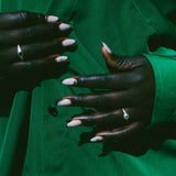Close-up of a person wearing a bright green button-up shirt, showing both hands with pale pink manicured nails and rings.
