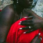 A close-up lifestyle shot of a model wearing a vibrant red strapless dress, sitting outdoors against a textured gray rock background.