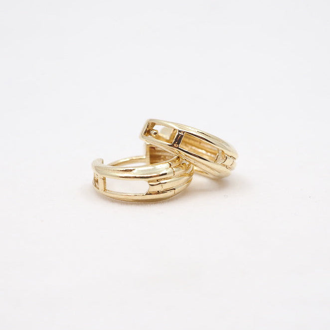 Two gold earrings on a light beige background