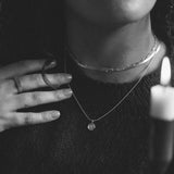 black and white photo of woman wearing two ilver chain necklaces and a silver zodiac pendant necklace