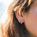 A close-up image of a person wearing sterling silver huggie hoop earrings, with the earrings visible against the earlobe.