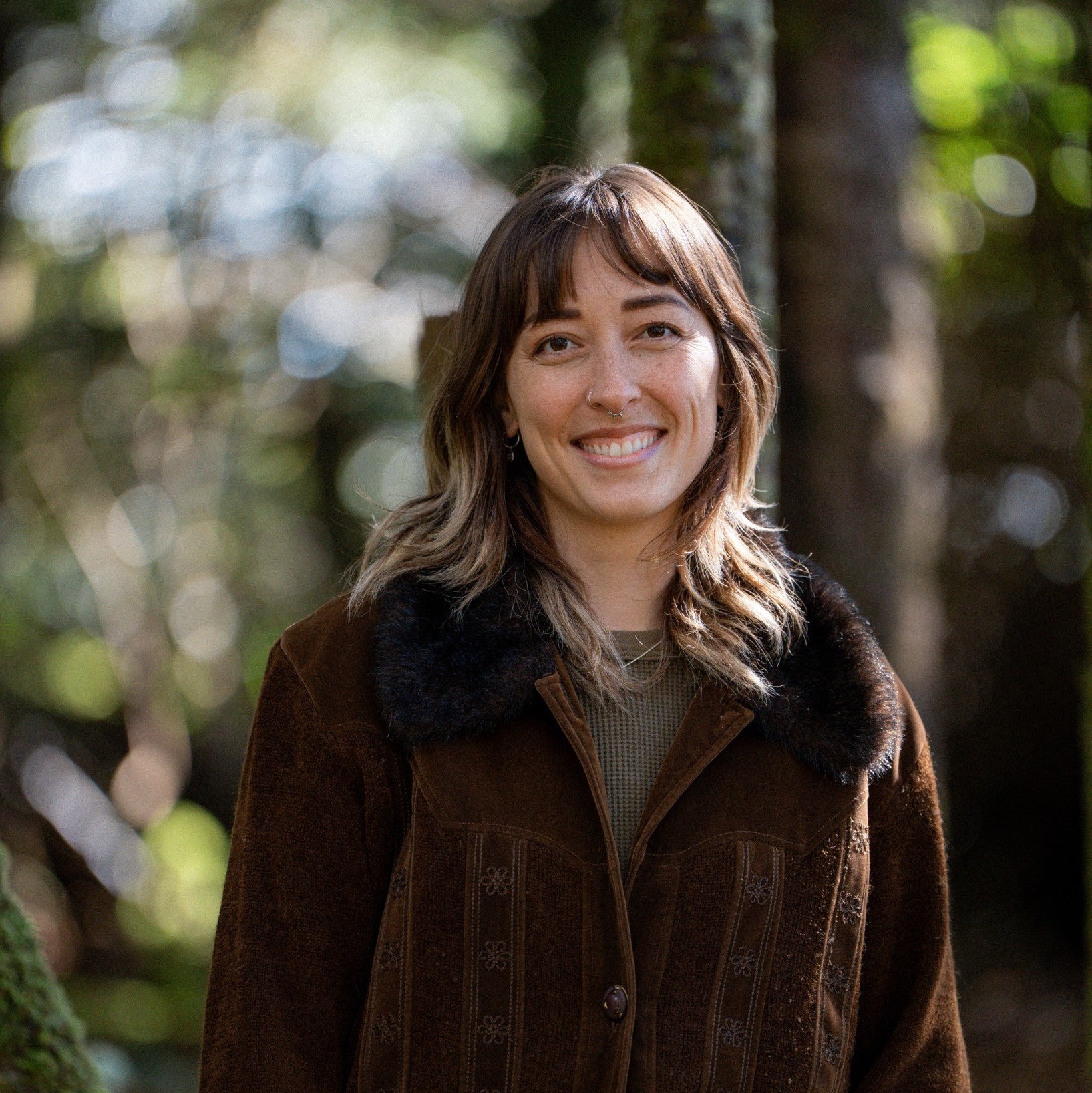 Woman wearing a brown coat with fur collar standing in a forest