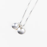 A close-up of a person's neck and chest wearing a delicate silver chain necklace with a small circular silver pendant.