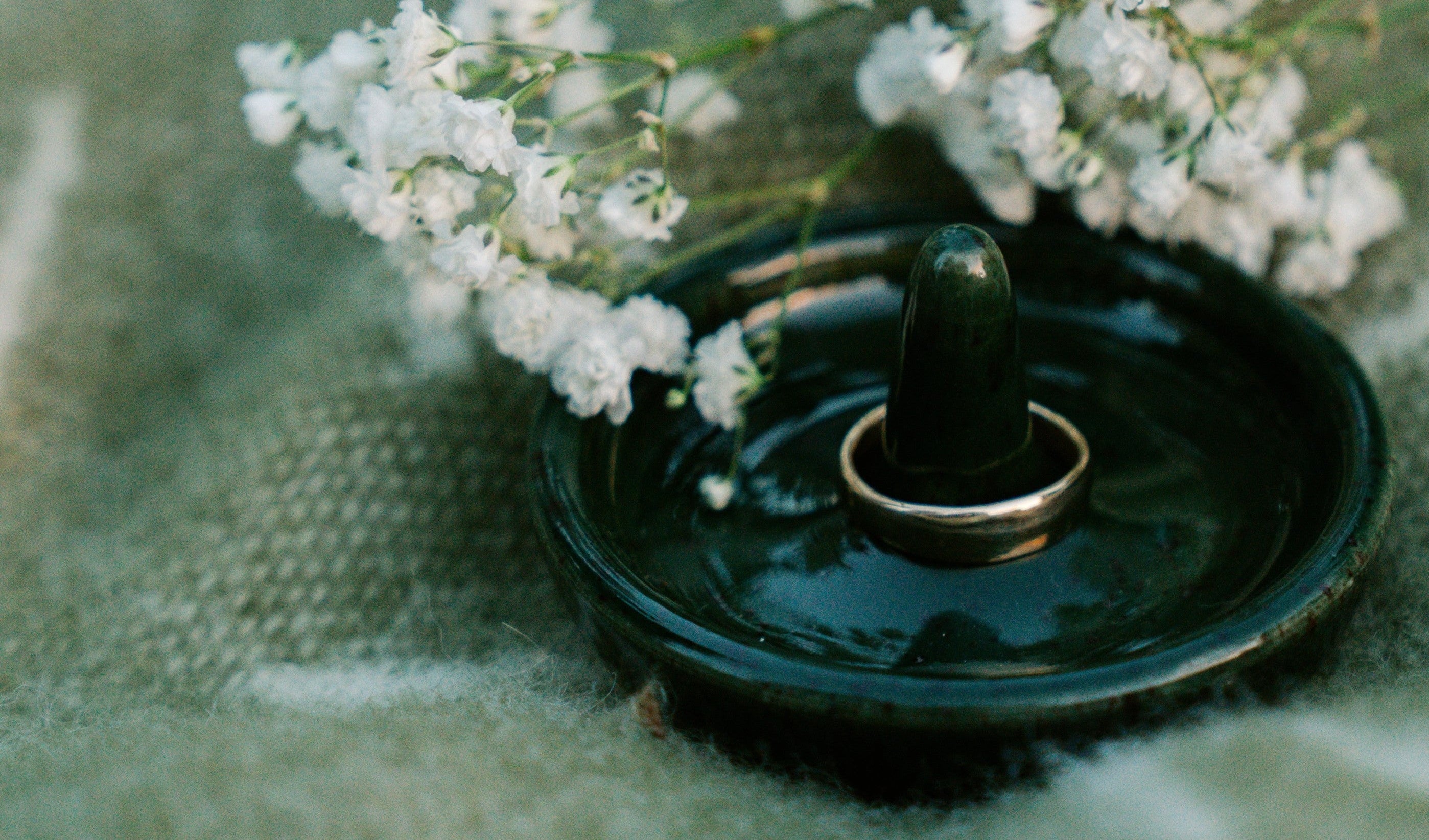 Small bouquet of white flowers on a dark green dish against a textured green background