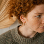 Person with red hair wearing a brown sweater and gold earrings.
