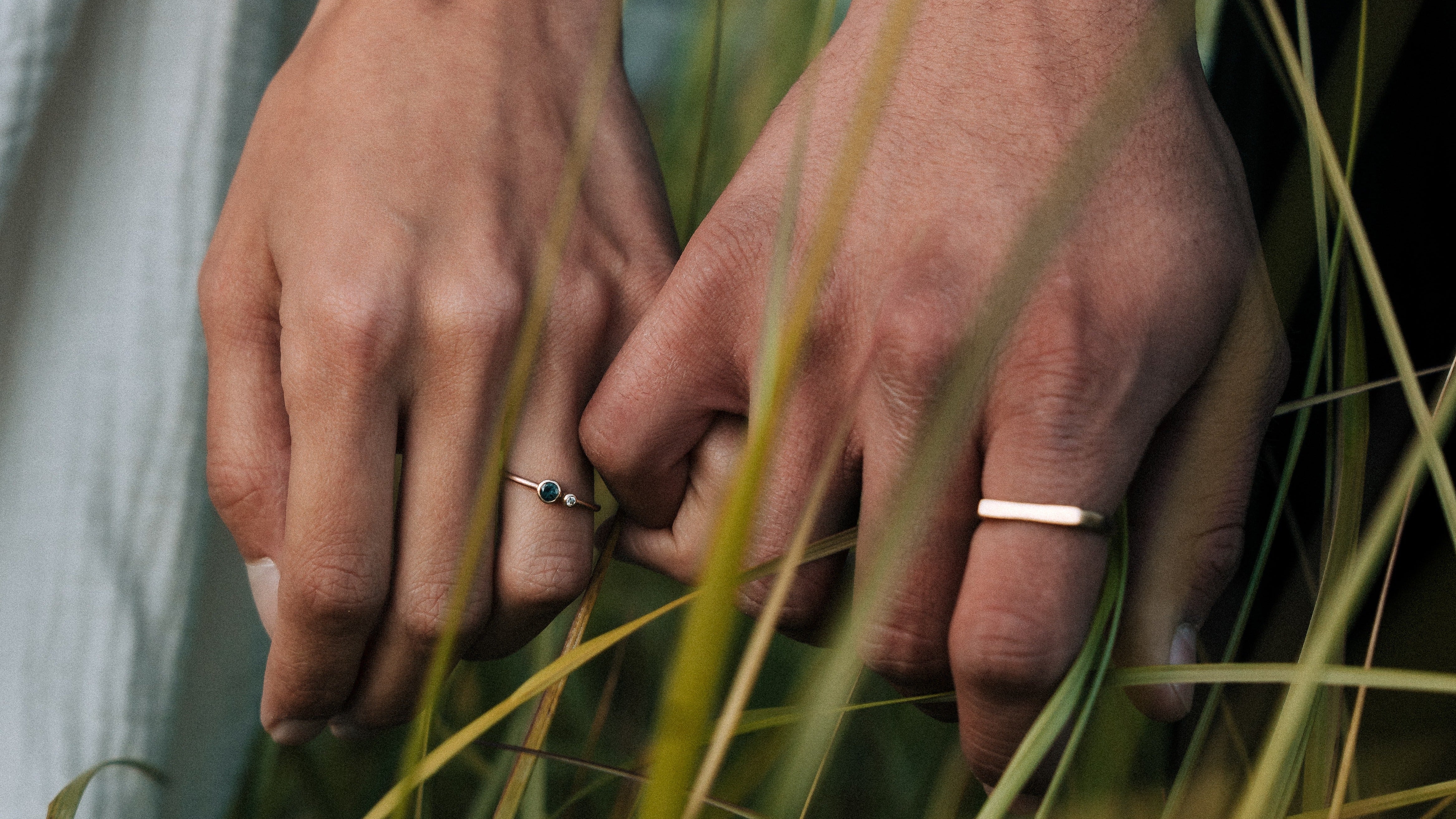 Close-up of two hands holding each other with grass in the foreground