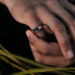 Hand wearing a ring with a green gemstone against a dark background