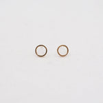 Two gold circle earring studs on a light gray background