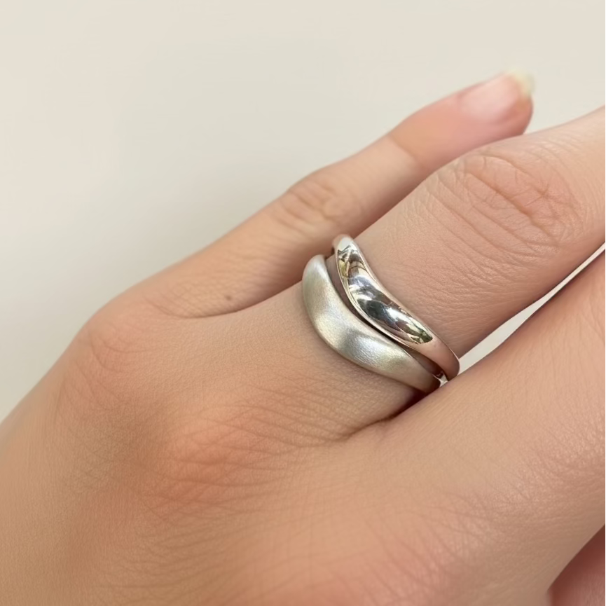 Silver ring on a finger against a plain background