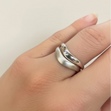 Silver ring on a finger against a plain background