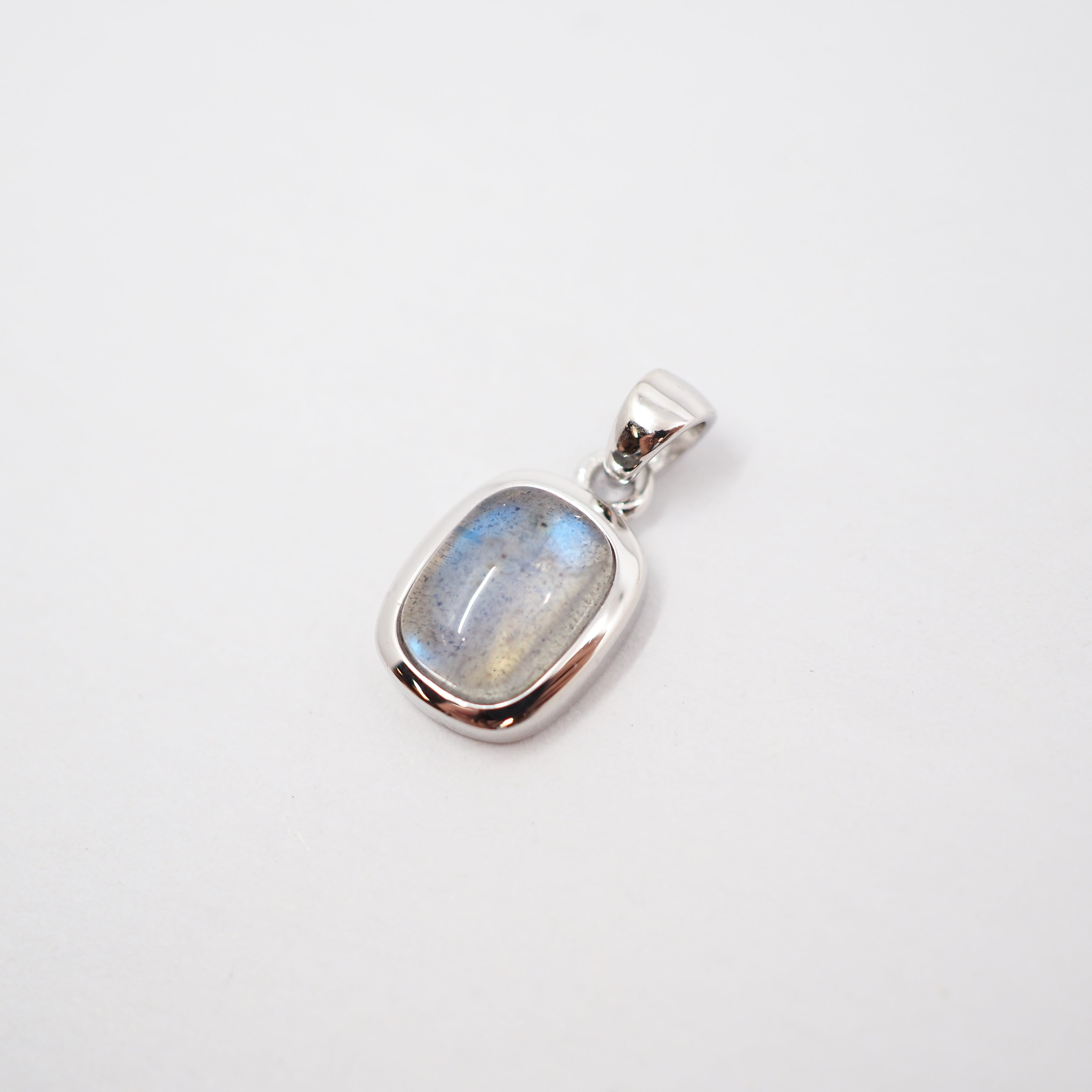 A close-up of a person wearing a delicate silver chain necklace with a small rectangular shaped pendant featuring a light blue-gray stone, styled with a dark brown knit cardigan.