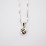 A silver box chain necklace with a small round bezel-set green gemstone pendant, shown against a plain white background.