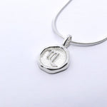 A silver necklace featuring a round pendant with a zodiac sign on it, attached to a delicate chain.