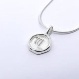 A silver necklace featuring a round pendant with a zodiac sign on it, attached to a delicate chain.