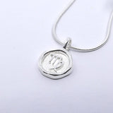 A silver necklace featuring a round pendant with a zodiac sign on it, attached to a delicate chain.