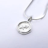 A silver necklace featuring a round pendant with a zodiac sign symbol on it, attached to a chain.